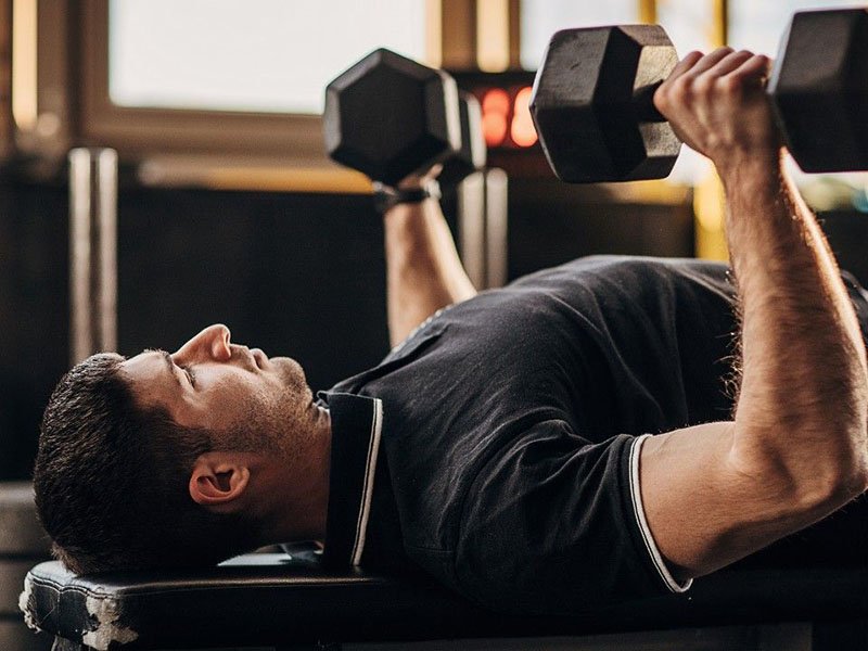the fitness trainer is doing some dumbbells exercise on flat bench