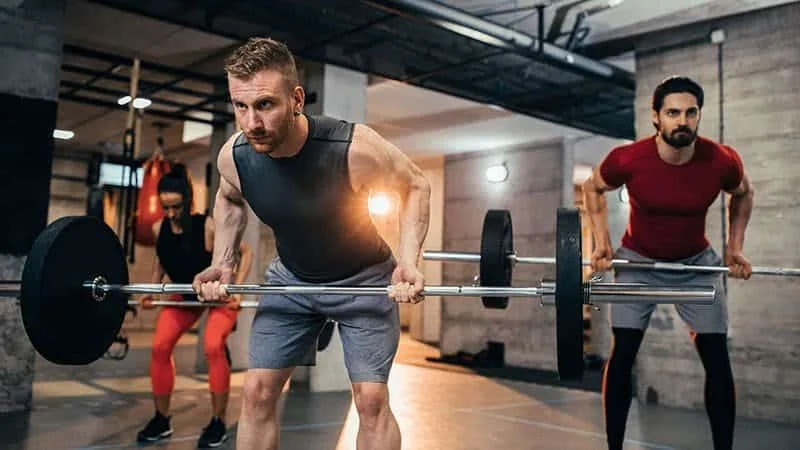 A beginner practicing barbell rows with an empty bar in a bright gym